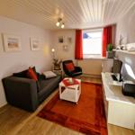 Living room with sofa, armchair, coffee table, and TV. Window with red curtains.