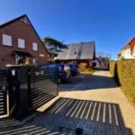 House with gate, paved path, parked cars under blue sky.