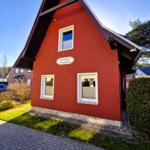Red holiday house with white windows and sign. Front garden with lawn and gravel.