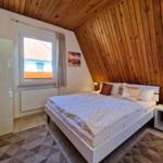 Bedroom with wooden wall, bed, and window with view of house