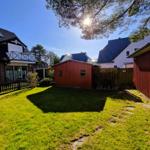 Red shed and green lawn in front of a house with balcony and tree.