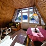 Living area with wooden ceiling, sofa, dining table with tablecloth, and window to balcony.