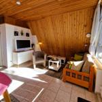 Living room with wooden wall, sofa, armchair, TV, and window.