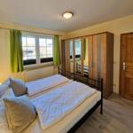 Bedroom with double bed, wooden wardrobe, and window with green curtains.