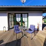 Terrace with table and two chairs, view into living area with green window frames.