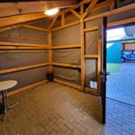 A room with wooden frame, brown floor, and an open door to the outside area.
