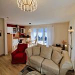 Living area with sofa, red armchair, and kitchen area in the background.