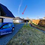 House with paved path, green lawn, and blue car. Sky with cloud.