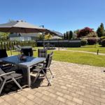 Terrasse mit Tisch, Stühlen und Sonnenschirm. Grasfläche und Zaun im Hintergrund.