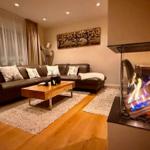 Ein Wohnzimmer mit Ledersofa, Holzfußboden und Kaminofen mit brennenden Holzscheiten.