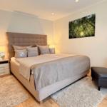 Schlafzimmer mit Bett, Nachttisch, Sessel und Wandbild.