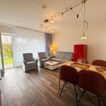 Wohn- und Essbereich mit Sofa, Stühlen und rotem Kühlschrank.