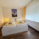 Schlafzimmer mit Doppelbett, Fenster mit Jalousien und Wandbild eines Leuchtturms.
