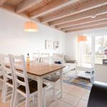 Dining area with table and chairs, living area with sofa and armchairs, wooden beam ceiling, large windows.