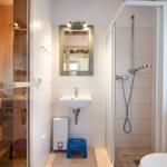 Bathroom with shower, sink, and sauna. Wooden frame and white tiles.