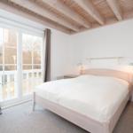 Bedroom with wooden beam ceiling, bed, nightstand, and window to terrace.