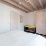 Bedroom with bed, wardrobe, and baby crib under wooden beam ceiling.