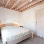 Bedroom with wooden floor, bed, and nightstands. Ceiling beams and door are visible.