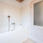 Bath with bathtub, showerhead, and wooden door