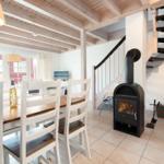 Dining room with wooden table, white chairs, and wood stove. Stairs lead upstairs.