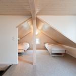 Two beds in an attic room with wooden ceiling and window.