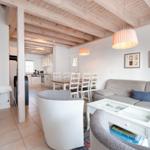 Living area with sofa, dining table, and kitchen under wooden beams.
