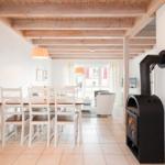 Dining room with wooden beams, dining table and chairs, wood stove, and view into the living room.