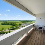 Balcony with table and chairs, view of green landscape and parking lot.