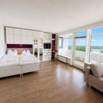 Room with double bed, sofa, and large window with view of the landscape.
