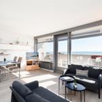 Wohnbereich mit Sofa, Esstisch und großem Fenster zum Meer.