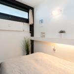 Schlafzimmer mit Bett, Fenster und Wandregal mit Pflanzen und Lampen.