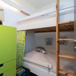 Ein Schlafzimmer mit Doppelstockbett, grünem Schrank und Vorhang.