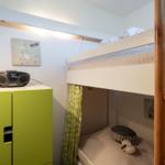 Ein Schlafzimmer mit Doppelstockbett, grünem Schrank und Wandbild mit Dinosaurier.