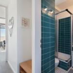 Badezimmer mit Dusche und Waschbecken. Blick auf Balkon mit Meerblick.