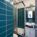 Badezimmer mit Dusche, Waschbecken und Toilette. Wände mit türkisen Fliesen verkleidet.