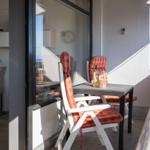 Terrasse mit Tisch, zwei Stühlen und Blick aufs Meer. Im Hintergrund Küche und Wanduhr.