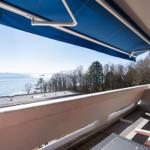 Terrasse mit Blick auf Meer und Bäume unter blauem Markisen.