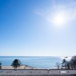 Blick auf einen Strand mit Bäumen und Meer unter blauem Himmel mit Sonne.