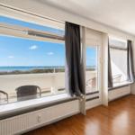 Room with sea view, balcony, wooden floor, and wall art.