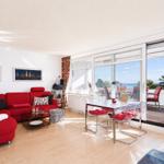 Living and dining area with red sofa, glass table, and balcony view of the sea.