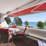 Terrace with table, chairs, and view of sea and trees.
