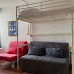 Ein Raum mit einem Hochbett, einem grauen Sofa und einem roten Klappstuhl.