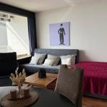 Zimmer mit Sofa, Bett und Tisch. An der Wand hängt ein Bild von Charlie Chaplin.