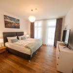 Schlafzimmer mit Doppelbett, Holzboden, TV und Fenster mit Vorhängen.
