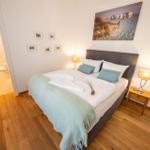 Schlafzimmer mit Bett, Nachttisch und Wandbild. Durchgang zur Badewanne.
