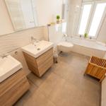 Badezimmer mit Dusche, Waschbecken und Toilette. Holzunterschränke und Fenster.