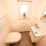 Badezimmer mit Toilette, Waschbecken und Fenster mit Pflanze.