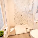 Badezimmer mit Dusche, Toilette und Fenster mit Jalousie.
