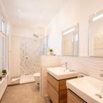 Badezimmer mit Dusche, zwei Waschbecken und Heizkörper