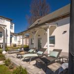 Terrasse mit Liegestühlen und Garten. Hinterhof mit Haus und Bäumen.